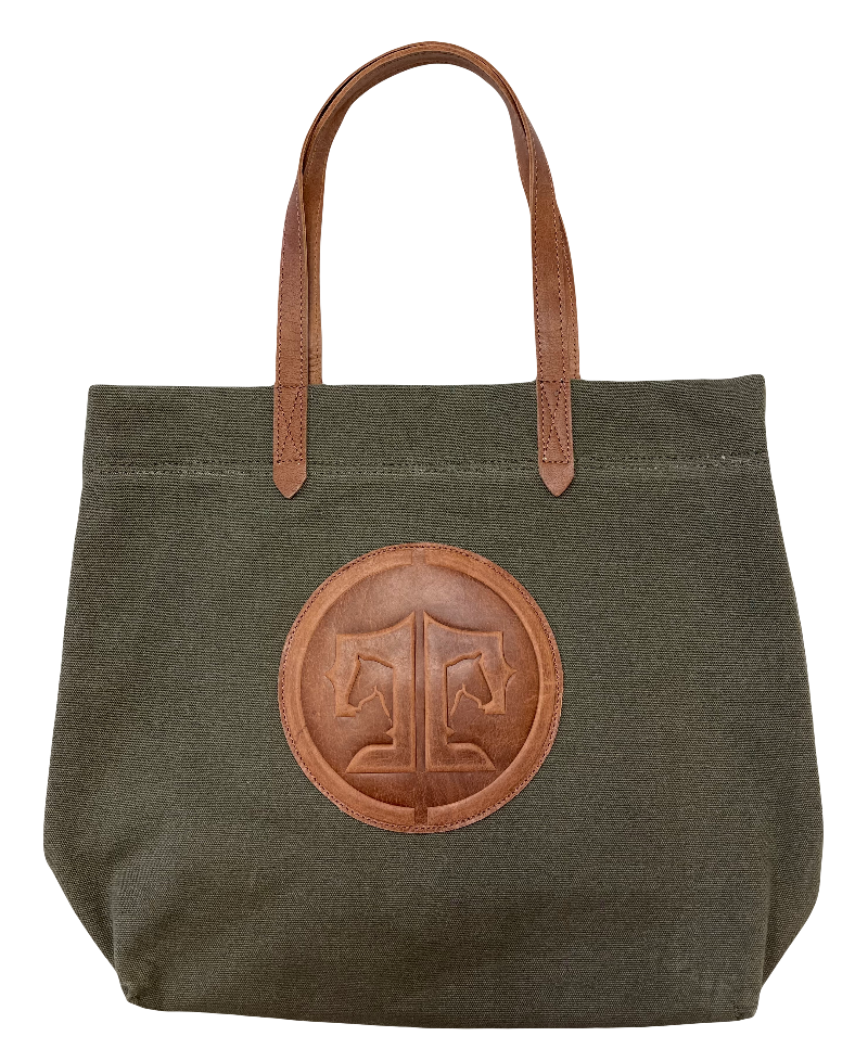 Green tote bag with brown leather handle and circular patch on a white background